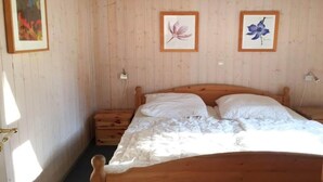 Ein Schlafzimmer mit einem hölzernen Bett, zwei gerahmten Blumenbildern, einem Nachttisch und einem Beistelltisch.