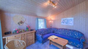 A cozy cabin interior with a wooden ceiling, a sofa, a dining table, a wicker chair, and a wall-mounted radio. - Ferienhaus mit Sauna im Ferienpark Mirow (Granzow)