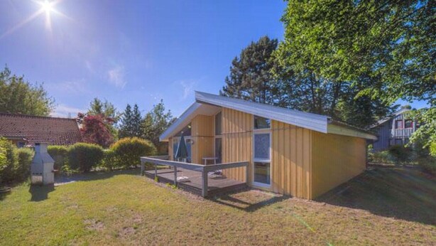 A single-story wooden house with a deck, surrounded by a grassy yard and trees. - Ferienhaus mit Sauna im Ferienpark Mirow (Granzow)