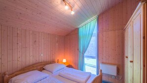 A wooden room with two beds, a window with curtains, a lamp, and a radiator. - Ferienhaus mit Sauna im Ferienpark Mirow (Granzow)