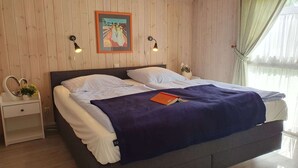 A bedroom with a wooden paneled wall, a bed with white bedding, a blue throw blanket, and two bedside lamps. - Ferienhaus mit Sauna im Ferienpark Mirow (Granzow)