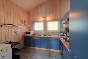 A compact kitchen with wooden walls, a blue countertop, and a window with curtains.