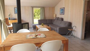 A cozy living area with a wooden table, two white chairs, a grey sofa, and a small table with a vase. - Ferienhaus mit Sauna im Ferienpark Mirow (Granzow)