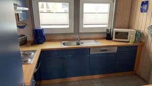 A modern kitchen with a sink, stove, and microwave. There are two windows above the sink and a clock on the wall. - Ferienhaus mit Sauna im Ferienpark Mirow (Granzow)
