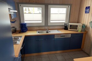 A modern kitchen with a sink, stove, and microwave. There are two windows above the sink and a clock on the wall. - Ferienhaus mit Sauna im Ferienpark Mirow (Granzow)