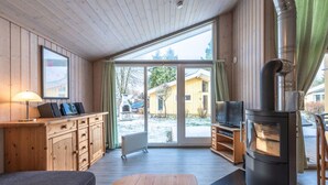 Ein gemütliches Blockhäuschen-Interieur mit Holzausstattung, einem großen Fenster, einem Kamin und einem Fernseher.
