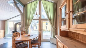 Ein Essbereich aus Holz mit Tisch und Stühlen, ein großes Fenster mit Vorhängen und Blick ins Freie.