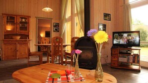 Ein gemütliches Wohnzimmer mit Holzmöbeln, einem Kamin, einem Fernseher und einem Fenster mit Vorhängen.