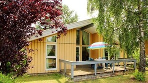 Una casa moderna de madera con terraza y un paraguas colorido.