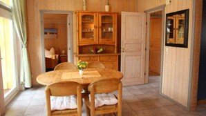 Ein Zimmer mit Holzwänden, einem Esstisch, Stühlen, einer Vitrine und einer Tür zu einem anderen Raum.