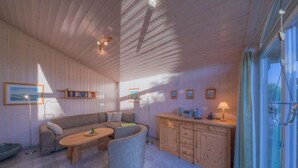 L’intérieur chaleureux d’un chalet avec un plafond en bois, un canapé, une table à manger et un coin cuisine.