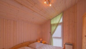 Une chambre à coucher aux murs lambrissés, avec un lit, une table de chevet, une lampe et une fenêtre avec des rideaux.