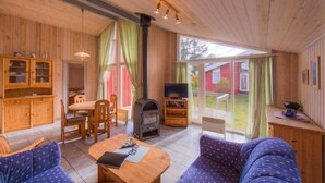 A cozy cabin interior with wooden walls, a dining area, a sofa, a television, and a fireplace. - Ferienhaus mit Sauna im Ferienpark Mirow (Granzow)