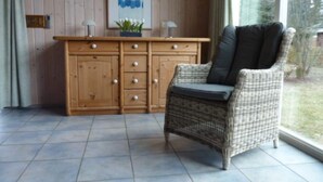 A wicker chair with a cushion in a room with a wooden cabinet and a window.