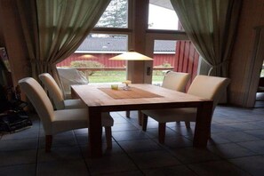 Enjoy meals in this dining area with a wooden table and four chairs, surrounded by large windows and a table lamp.