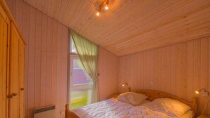 Ein Zimmer mit Holzwänden, einem Bett, einem Fenster mit Vorhängen und einem Heizkörper.
