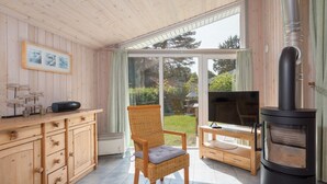 Ein gemütliches Zimmer mit einem Holzkasten, einem Korbstuhl, einem Fernseher und einem Kaminofen.