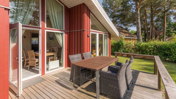 Ein zweistöckiges Haus mit einer Terrasse, großen Fenstern und einem Essbereich mit Gartenmöbeln.