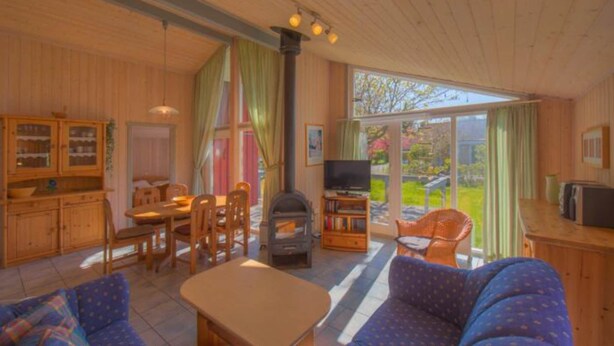 A cozy cabin interior with a dining area, a sofa, a television, and a fireplace. - Ferienhaus mit Sauna im Ferienpark Mirow (Granzow)