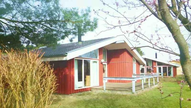 Ein rotes Gebäude mit einem geneigten Dach und großen Fenstern, umgeben von Gras und Bäumen.