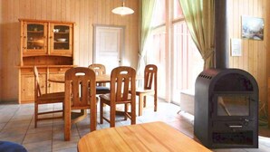 Ein Holzinterieur mit Esstisch und Stühlen, einer Schranke mit Glastüren und einem Holzofen.