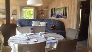 Ein gemütliches Zimmer mit einem runden Esstisch, gedeckt für vier Personen, einem blauen Sofa und einem großen Waldgemälde.