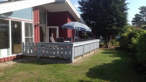 Ein Haus mit einer Terrasse, einer Veranda mit gestreifter Sonnenschirm und einem Rasen.