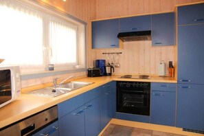 A kitchen with blue cabinets, a microwave, a sink, a stove, and a window with curtains.