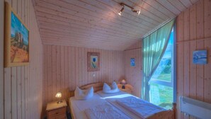 Ein Schlafzimmer einer Holzhütte mit einem Bett, einem Nachttisch und einem Fenster mit Vorhängen.