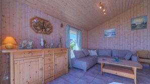 Ein gemütliches Blockhaushaus-Interieur mit einem Holzschrank, einem grauen Sofa, einem Holztisch und einem Fenster mit Vorhängen.