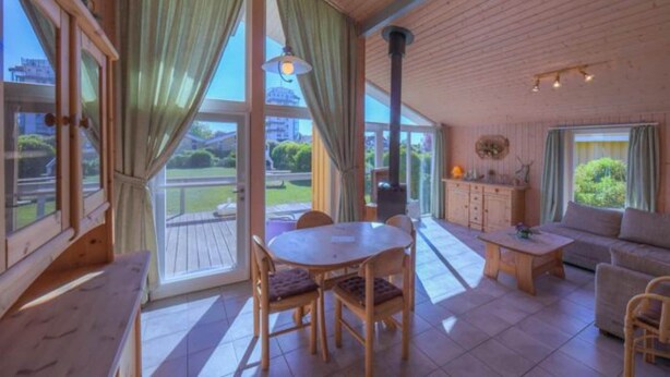 Ein geräumiges Zimmer mit Holzboden, großen Fenstern mit Vorhängen, einem runden Tisch mit Stühlen, einer Couch und einem Schrank.