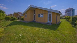 Eine Reihe von gelben Holzhäusern mit flachem Dach, umgeben von grünem Gras und Büschen.