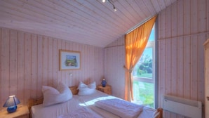 A bedroom with a wooden ceiling, a bed with white bedding, a nightstand with a lamp, and a window with curtains.