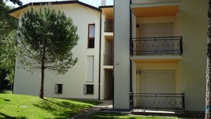 Ein zweistöckiges Gebäude mit flachem Dach, einem kleinen Baum davor und einem Balkon mit dekorativen Geländern.