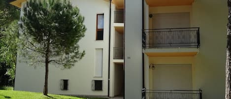 A two-story building with a flat roof, a small tree in front, and a balcony with decorative railings.