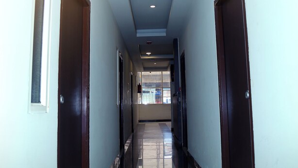 A long, narrow hallway with dark wooden doors on either side and a tiled floor. - MR DWELL HOTEL AIRPORTZONE (Hyderabad)