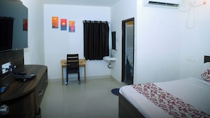 A hotel room with a bed, a desk with a computer, a chair, a window with curtains, an air conditioning unit, and a wall-mounted TV. - MR DWELL HOTEL AIRPORTZONE (Hyderabad)