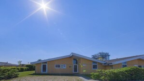 Un edificio moderno con tetto piatto e ampie finestre, immerso nel verde sotto un cielo azzurro intenso.
