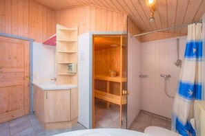 A wooden cabin bathroom with a shower, a toilet, and a sink.