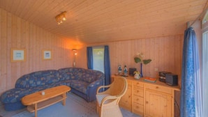 L’intérieur chaleureux d’un chalet avec un plafond en bois, un canapé, un fauteuil, une petite table et un bureau avec une radio.
