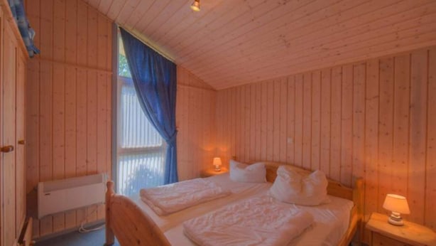 Une chambre dans une cabane en bois, avec deux lits, une fenêtre ornée de rideaux bleus et une table de chevet avec une lampe.