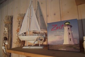 A book titled "Zeit meiner Traume" with a lighthouse illustration on the cover, placed on a wooden shelf next to a model sailboat. - Ferienhaus im skandinavischen Stil (Rechlin)