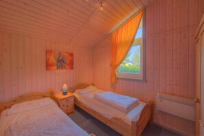 A room with two wooden beds, a nightstand with a lamp, a painting on the wall, and a window with curtains.