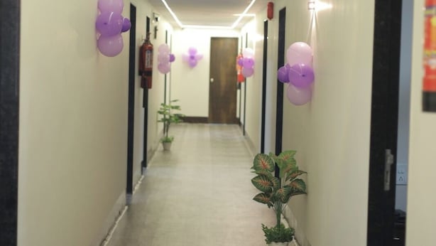 A hallway with a tiled floor, walls with doors, and purple balloons. - The Grand Vinayak Hotel (Surat)