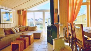 Ein gemütliches Zimmer mit Holzboden, einer Couch, einem Tisch und einem großen Fenster mit Vorhängen.