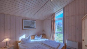 A wooden-paneled room with a bed, a nightstand, a window with curtains, and a door.