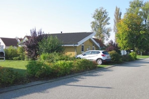 A residential street with houses, a parked car, and greenery.