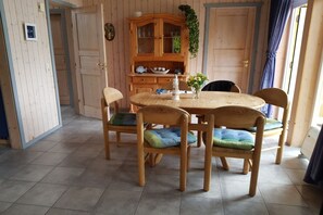 A dining area with a wooden table and chairs, a cabinet with glass doors, and a potted plant.