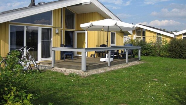 A modern yellow building with a covered patio, large windows, and a chimney. - Ferienhaus im skandinavischen Stil (Rechlin)