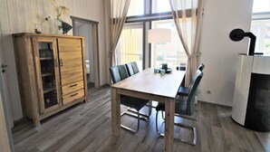 A dining area with a wooden table and chairs, a cabinet with glass doors, and a large window with curtains. - Ferienhaus im Ferienpark Mueritz (Rechlin)